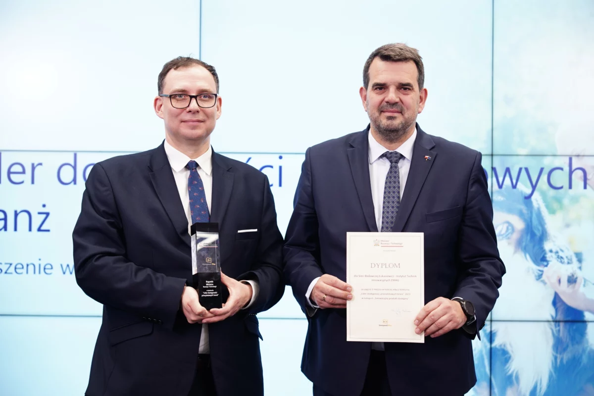 Dwaj mężczyźni w garniturach. Jeden trzyma statuetkę, drugi dyplom