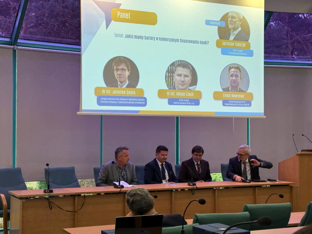 4 mężczyzn siedzących przy  długim stole na scenie