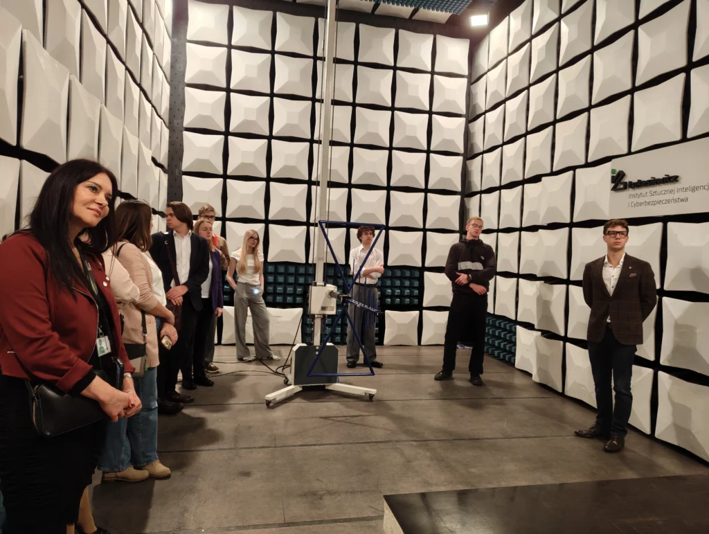 Grupa osób w dużym pomieszczeniu wyłożonym płytami na ścianach