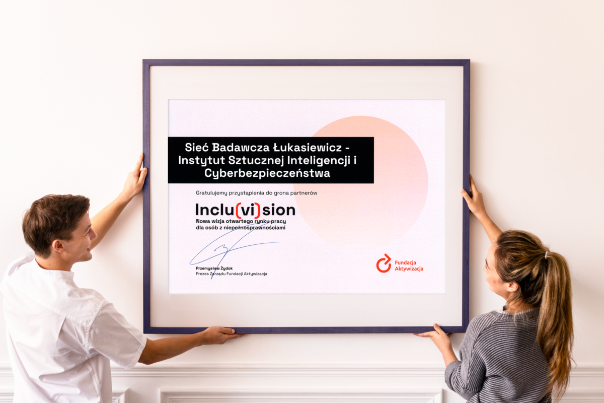 Mężczyzna i kobieta wieszają w ramie na ścianie certyfikat Incluvision dla Łukasieiwcz AI