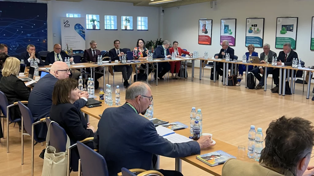 Liczna grupa uczestników oficjalnego spotkania siedzi na dużej sali przy stołach ułożonych w podkowę