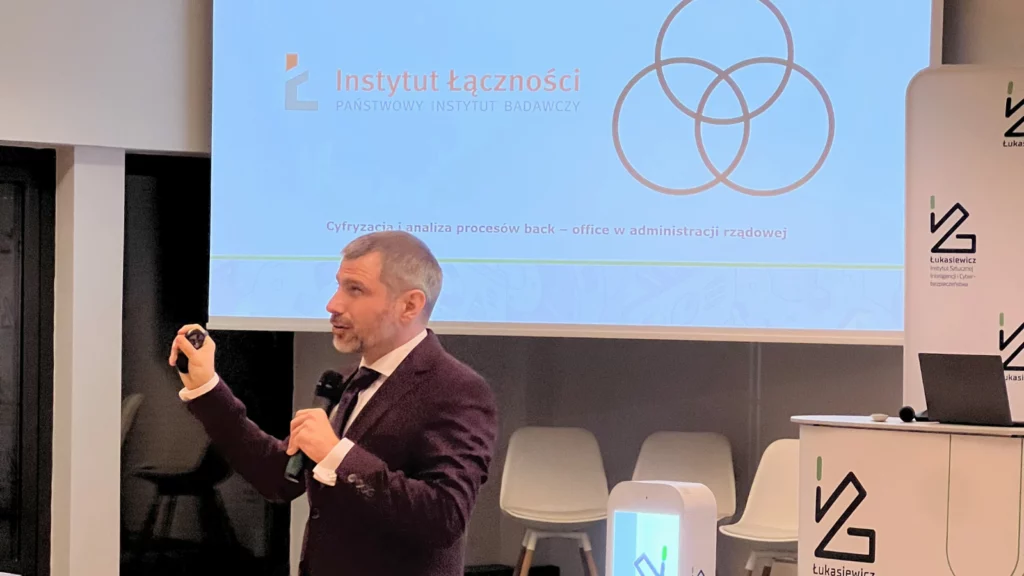 Mężczyzna w garniturze przemawia trzymając mikrofon na scenie 